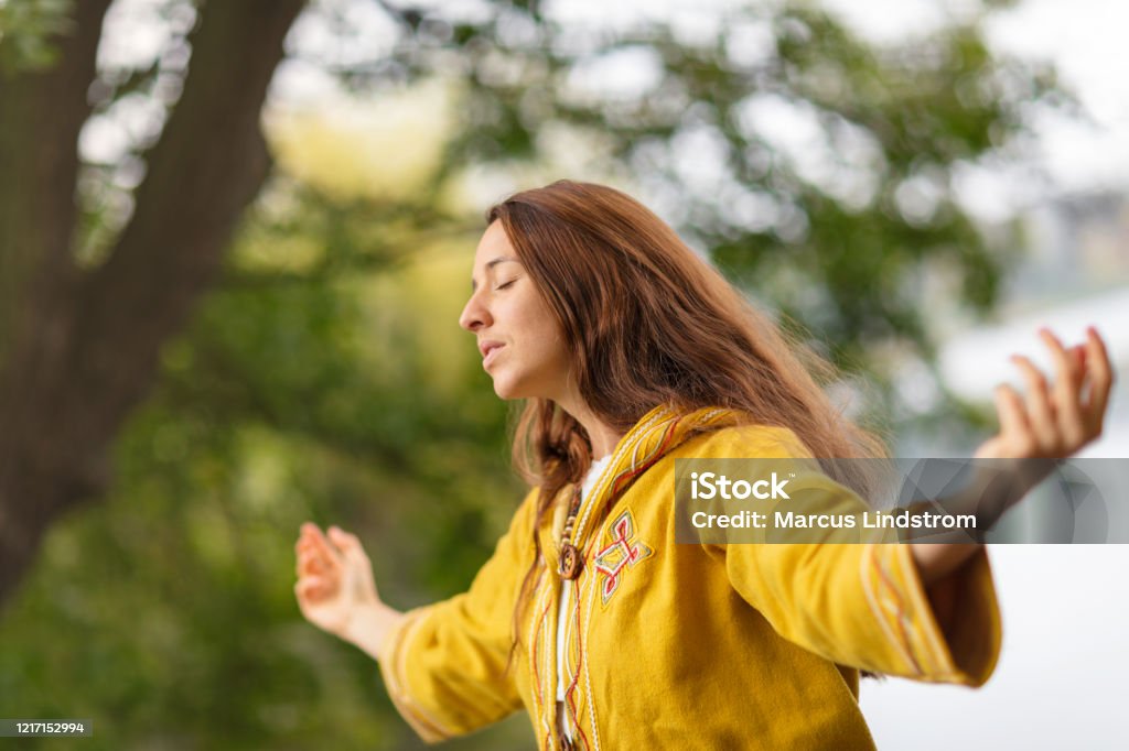 A woman meditating in nature A woman meditating in a forest environment with her arms outstretched. Chanting Stock Photo