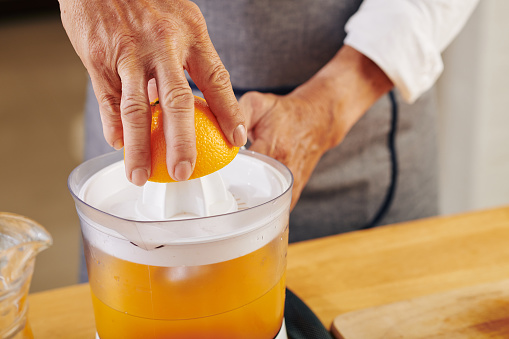 Close-up image of mature man squeezing orange fruit and making fresh juice for breakfast