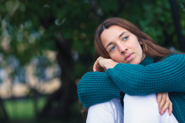 A young woman in thoughts sitting curled up outdoors.