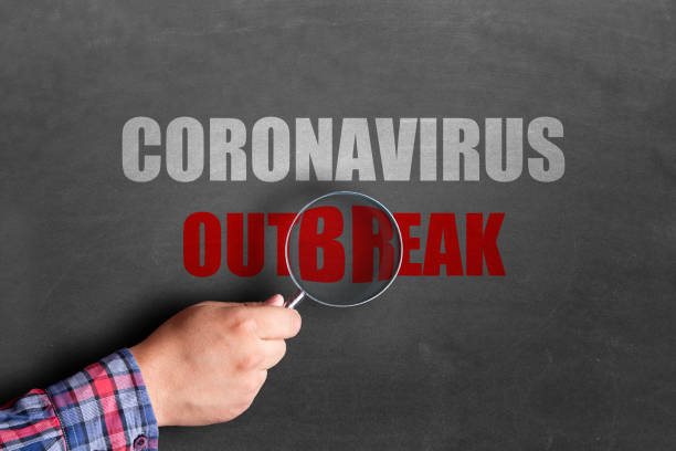 istock Man holding magnifying glass over coronavirus outbreak text on blackboard 1217154939