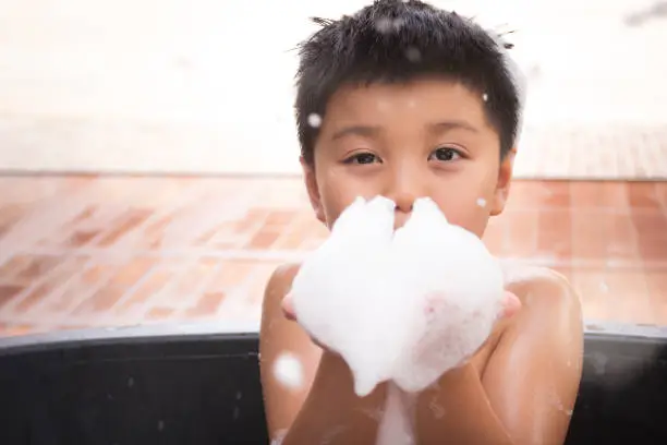 Photo of Asian boy is bathing in a tub.Child hands holding a soap foam