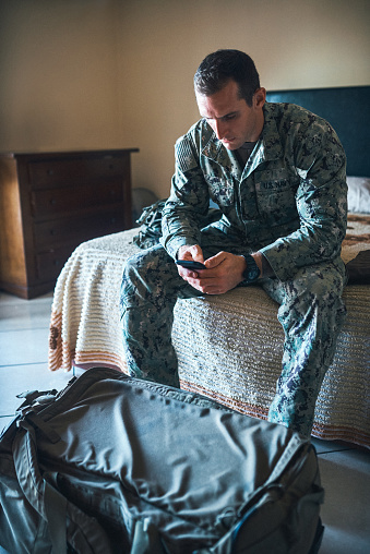 Shot of a young soldier sitting on his bed and using a smartphone
