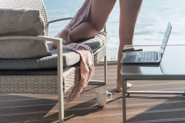 pattes femelles enveloppées dans un plaid près d’un canapé et bronzer sur la terrasse avec une tasse de café le jour d’été. vue sur la mer. wfh. travailler à domicile - knitting residential structure glasses hot drink photos et images de collection