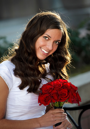 A happy young woman in a wedding dress sitting outdoors.