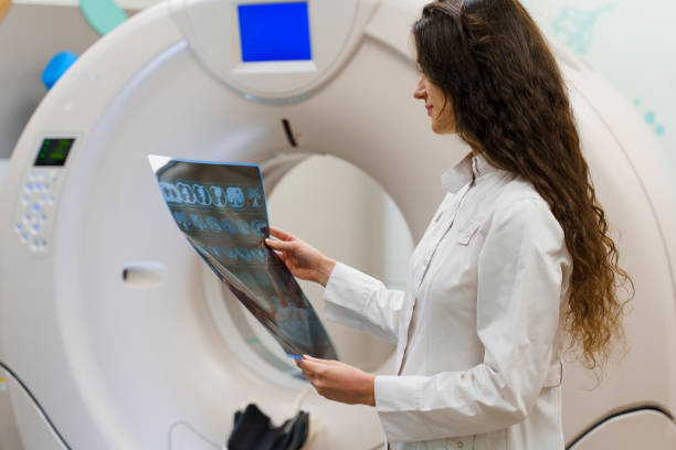 el estudiante de medicina examina la imagen de rayos x del cerebro del paciente cerca de la tomograhfina de kt komputer. joven en clínica médica tiene nueva experiencia - cat scan abdomen medical scan x ray fotografías e imágenes de stock