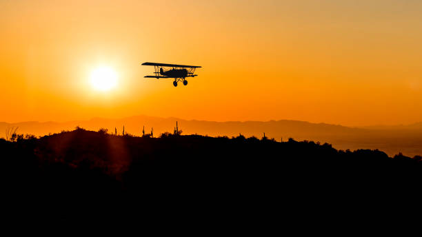 Bi-plane flying over desert at sunset