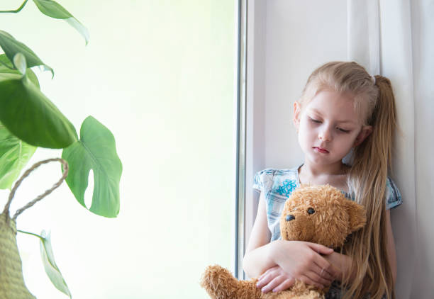 istock Sad child girl by the window 1217163199