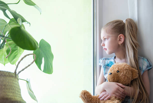 istock Sad child girl by the window 1217163204