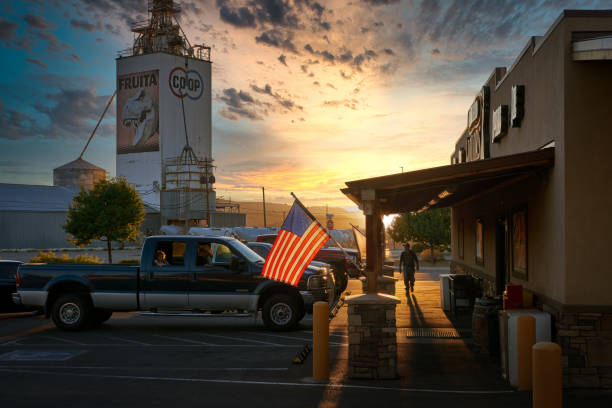 Sunset at the liquor store in Fruita Colorado, USA Beautiful sunset scene. Parked pikap track by the American flag, man walks on porch towards liquor store in Fruita, Colorado. In the background a tower with the emblem of the city: a T-rex. fruita colorado stock pictures, royalty-free photos & images