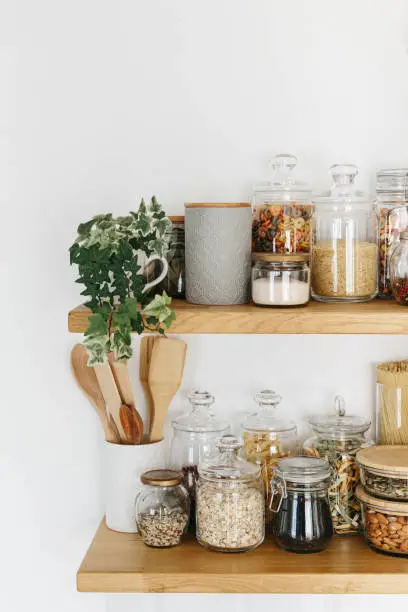 Photo of Various cereals and seeds in glass jars on the shelves in the kitchen. Kitchen interior ideas. Eco friendly kitchen, zero waste home concept