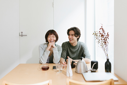 Young couple sitting behind the kitchen table, laughing and enjoying the time spent together.