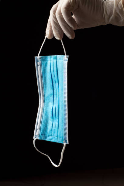 istock sanitary mask with one blue face and the other white with two elastic bands, held by one hand with a clear sanitary glove 1217174304