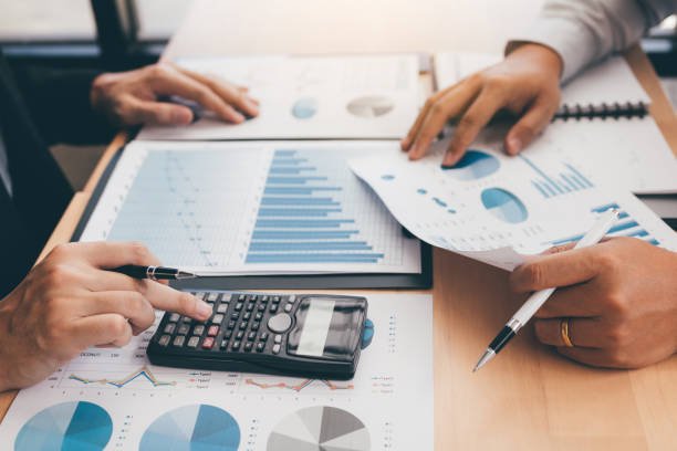 istock Two business people analyzing summary graph reports of business operating expenses and using calculator profit calculation in the office. 1217176914