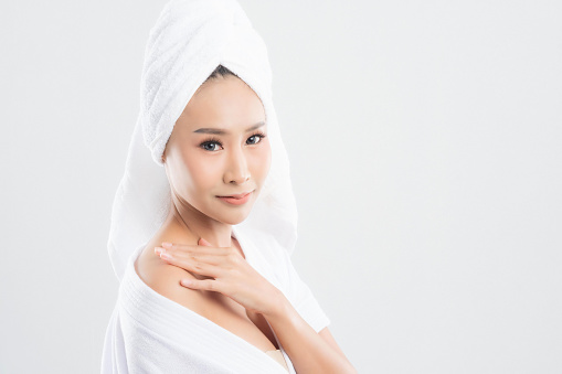 Beautiful young woman in bath towel is touching her face and smiling isolated on white background. Woman after bath with clean perfect skin.