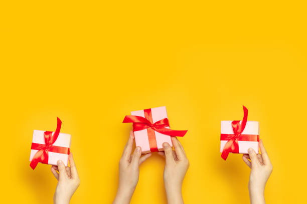 istock Human hands holds surprise boxes with red bow on a yellow background, top view 1217179007