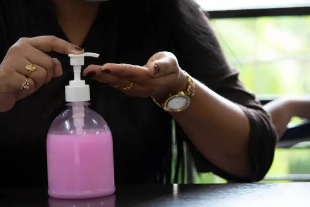 Midsection of woman pouring handwash sanitizer on her palm to clean and protect self from infectious coronavirus disease