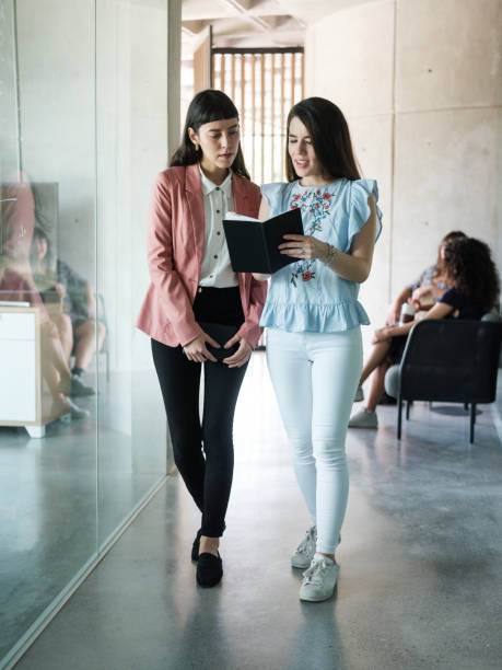 istock Two beautiful young women reading from notebook at work 1217180869