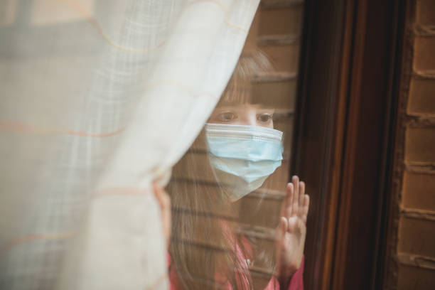 istock Child with mask looking through the window. 1217181264