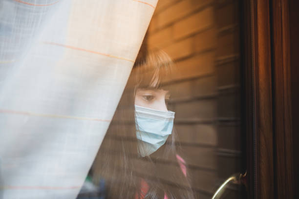 istock Child with mask looking through the window. 1217181280