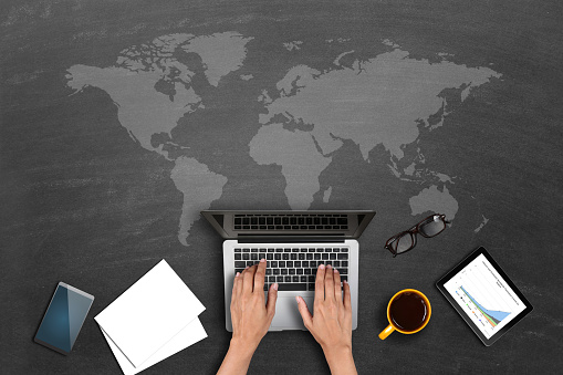 Businesswoman working on laptop over blackboard with world map