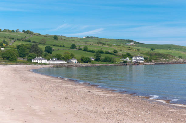 Cushendun Beach View North Northwest Cushendun (from Irish: Cois Abhann Doinne, meaning "foot of the River Dun") is a small coastal village in County Antrim, Northern Ireland. It sits off the A2 coast road between Cushendall and Ballycastle. It has a sheltered harbor and lies at the mouth of the River Dun and Glendun, one of the nine Glens of Antrim. Seen here is the beach, harbor, Torr Road climbing distant hills of the Antrim coast. Cushendun is part of Causeway Coast and Glens district.  Cushendun Caves are featured in the "Game of Thrones" series. cushendun michael stephen wills stock pictures, royalty-free photos & images
