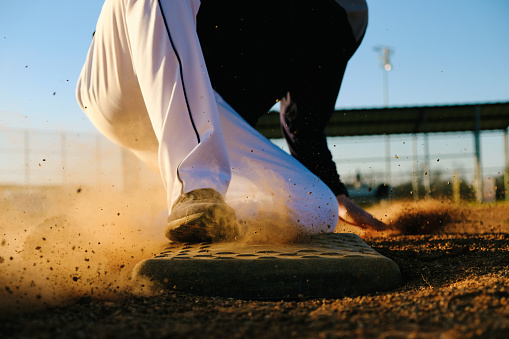 Baseball player lifestyle shows athlete sliding into base on field, sports action shot.