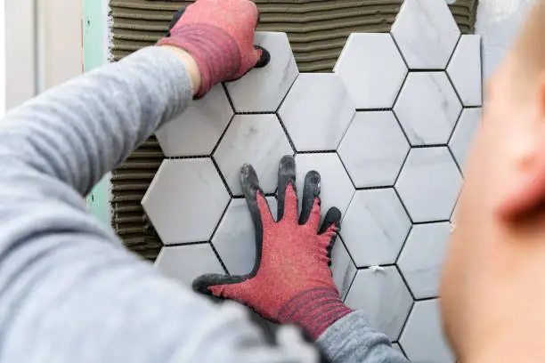 Photo of tiling - man laying marble texture hexagon tiles on the wall