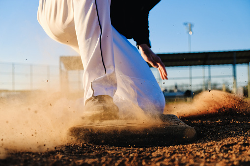Sports action shot of baseball player sliding into base on field, dirt in motion close up. Athlete lifestyle image.