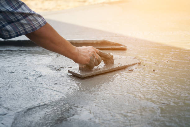 istock Close up of construction worker's gloved hands using trowel to scrape excess mix level with wood forms freshly poured concrete pad 1217190875