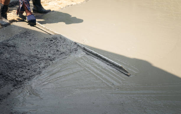 istock Close up of construction worker's gloved hands using trowel to scrape excess mix level with wood forms freshly poured concrete pad 1217190887