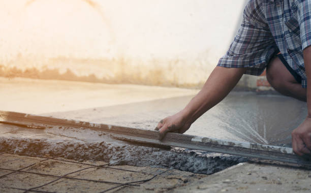 istock Close up of construction worker's gloved hands using trowel to scrape excess mix level with wood forms freshly poured concrete pad 1217190902