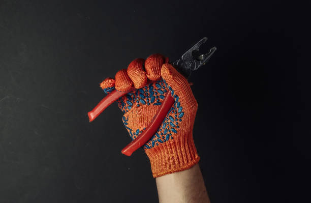istock Hands with work gloves are holding pliers on black background. Industrial worker 1217192354