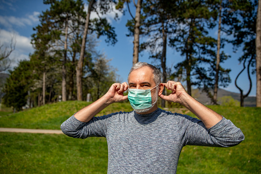 Mature Man Removing Protective Mask From his Face Outdoors in Public Park.