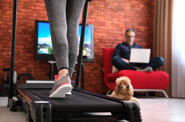 The man is working remotely. Woman exercising on a treadmill at home. stock photo