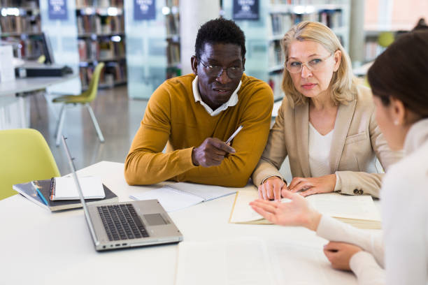 istock Female tutor helping students preparing for exam in library 1217198347
