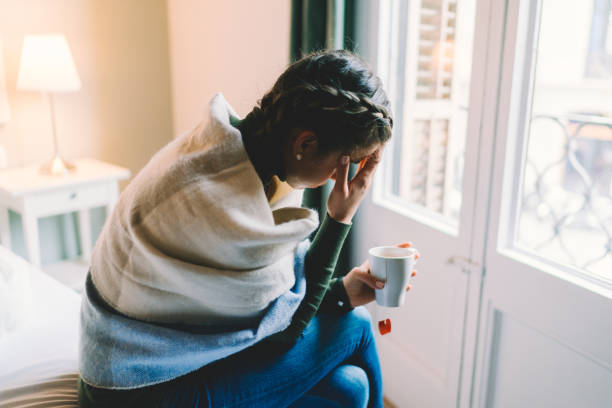 Staying home with flu virus Woman with temperature staying home wrapped in scarf and drinking hot tea symptoms stock pictures, royalty-free photos & images