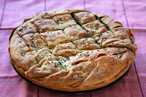 Healthy greek food concept. Whole spinach pie with sesame seeds or greek spanakopita with phyllo on kitchen table background.