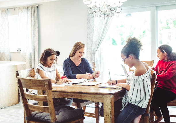 istock Mother of three supervises her school age daughters at home doing distance learning or schoolwork 1217200949