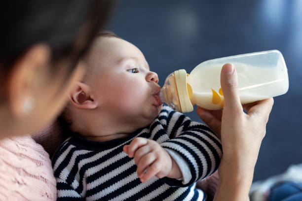istock Mother feeding her baby son with feeding bottle while sitting on sofa at home. 1217202929