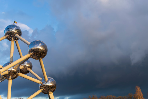 The Atomium Monument In Brussels with dark dramatic sky and with National Flag on the top