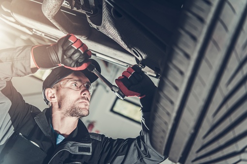 Modern Car Suspension Maintenance. Caucasian Automotive Technician in His 30s Fixing Vehicle Suspension Elements.