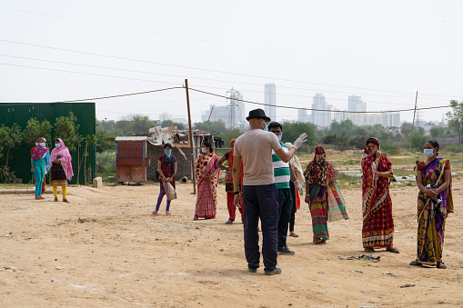 Gurgaon, Delhi, India - circa 2020 : Underprivileged women in sarees stand in a ilne following the social distancing norms to collect food rations at a donation drive. The coronavirus pandemic has resulted in a lockdown of the country leaving people without a livelihood and depending on social handouts for survival