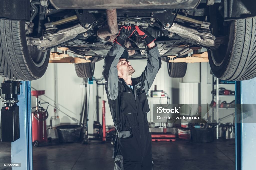 Mechanic Fixing Car on a Lift Caucasian Car Mechanic Under Vehicle Looking For Potential Issues with a Drivetrain. Automotive Industry. Car Stock Photo