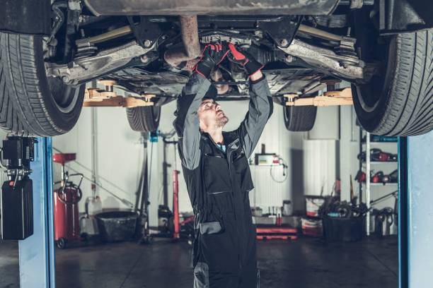 Mechanic Fixing Car on a Lift Caucasian Car Mechanic Under Vehicle Looking For Potential Issues with a Drivetrain. Automotive Industry. mechanic working under car stock pictures, royalty-free photos & images