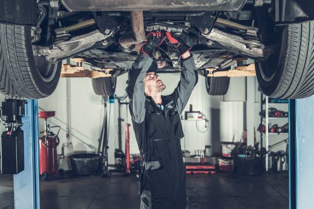 Mechanic Fixing Car on a Lift Caucasian Car Mechanic Under Vehicle Looking For Potential Issues with a Drivetrain. Automotive Industry. car repair stock pictures, royalty-free photos & images