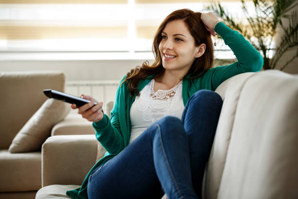 Smiling young woman watching TV during COVID-19 pandemic Smiling young woman watching TV during COVID-19 pandemic cable tv stock pictures, royalty-free photos & images