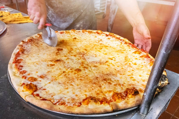 Pizzaiolo em Nova York cortando uma pizza de queijo gigante para tirar - foto de acervo