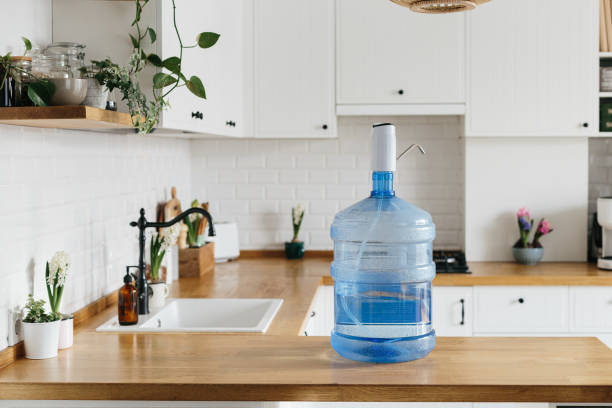 A larger bottle of clean water 19 liters with automatic white pomp in the interior of the apartment with a white kitchen in the background. stock photo