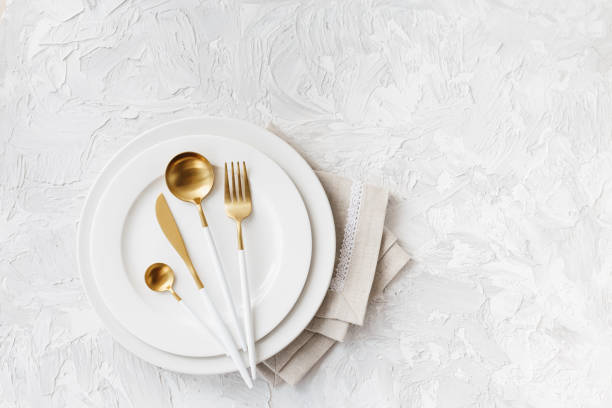 istock Beautiful gold and white cutlery on white plate on light white gray background 1217218064