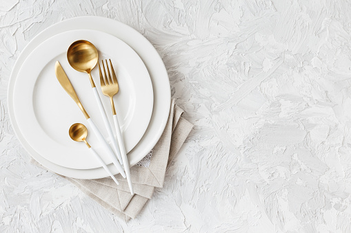 Beautiful gold and white cutlery - fork, knife, spoon on white plate on light white gray background. Flat-lay, top view. Copy space for your text.
